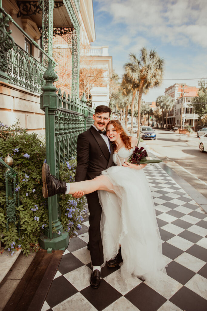 newly weds smiling while man is holding up her leg to show off her boots in Downtown Charleston