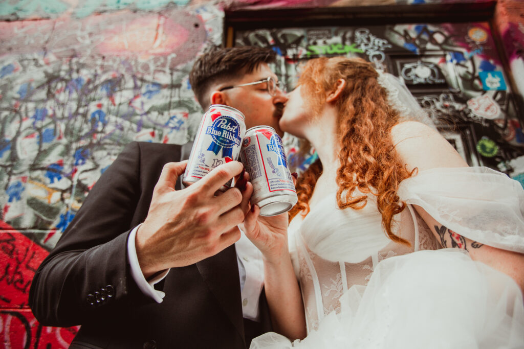 newlyweds holding up 2 cans of PBR at Recovery Room Tavern while kissing