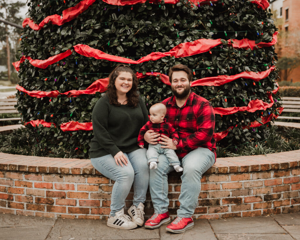 family Christmas photo in front of an ever green wrapped in red ribbon