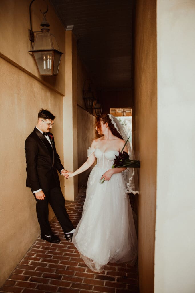 A wedding couple holding hands in a narrow brick-paved passage beneath a hanging lantern in historic Charleston.