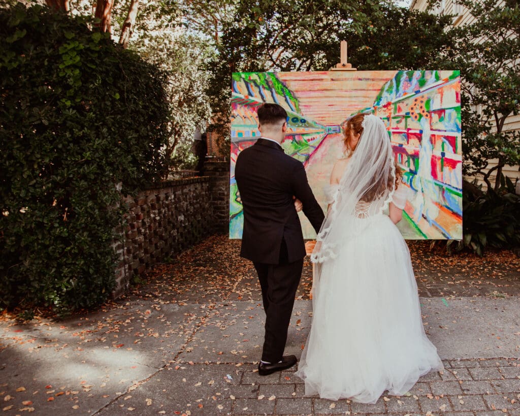 A newly married couple holding hands while looking at colorful outdoor artwork along a brick walkway.