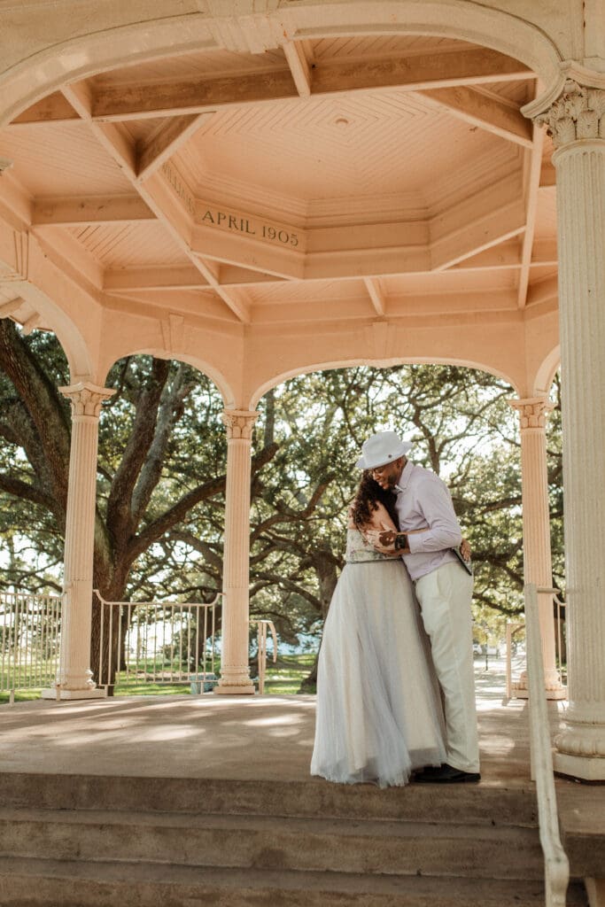 A wedding couple embracing inside the white gazebo at White Point Garden in downtown Charleston.