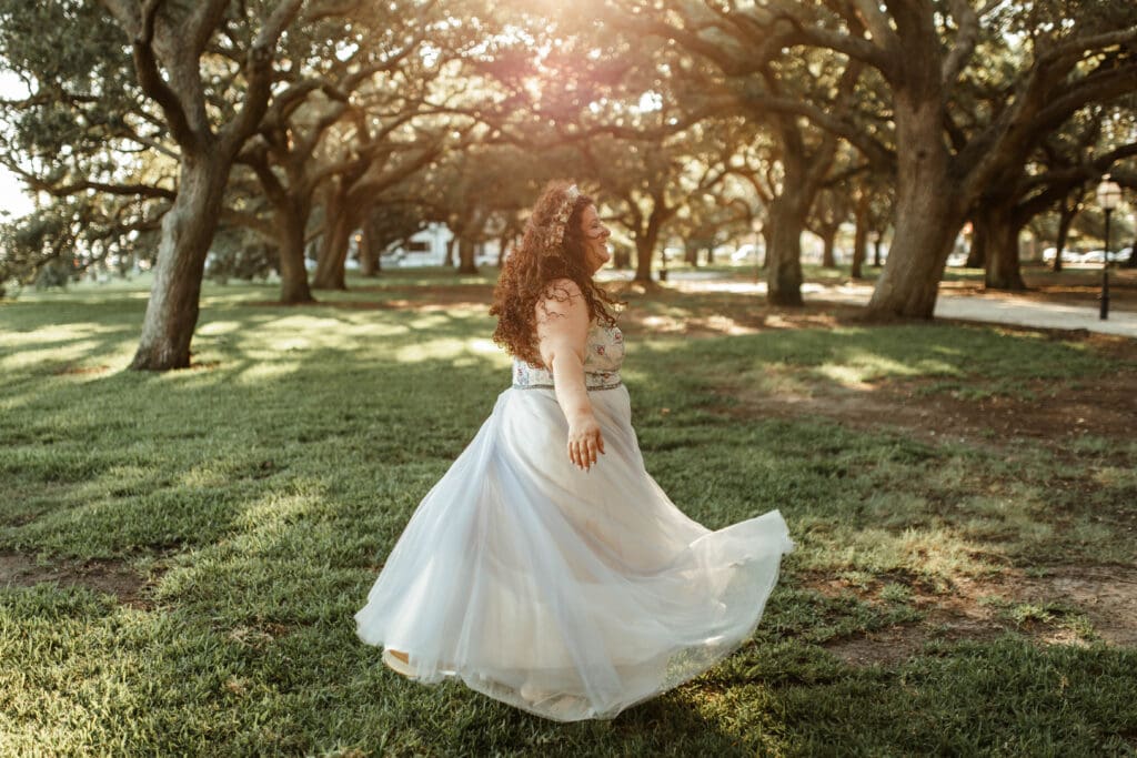 A bride twirling in a flowing wedding dress beneath sunlit oak trees at White Point Garden.