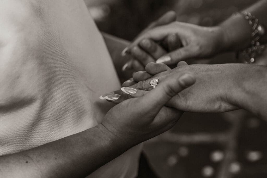 Black and white close-up of an engagement ring as the couple holds hands.
