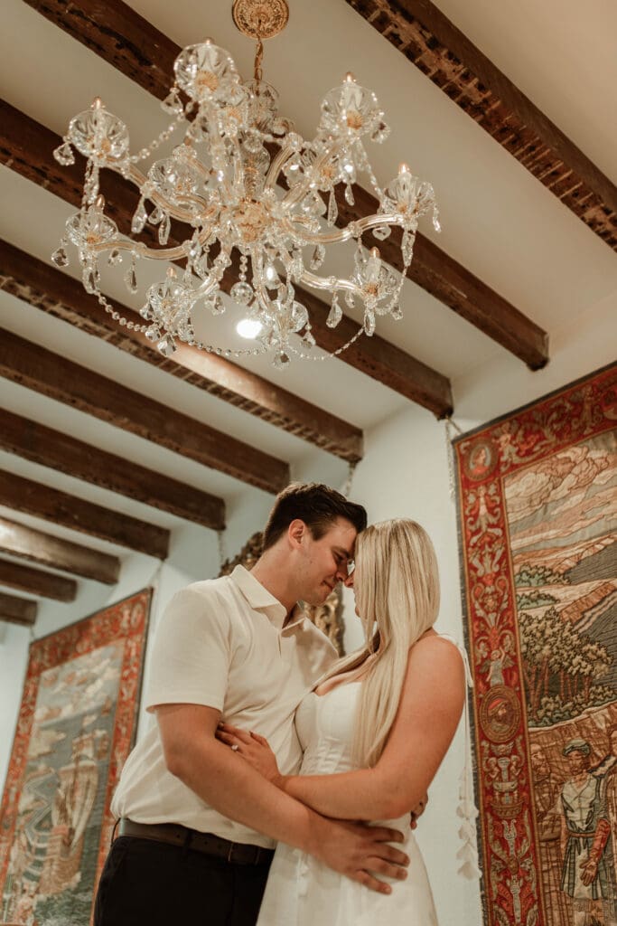 A newly engaged couple embracing beneath a crystal chandelier in the lobby of Charleston’s historic 20 South Battery.